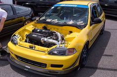 a yellow car parked next to other cars in a parking lot with it's hood open