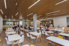 people are sitting at tables and eating food in the cafeteria with wooden ceiling beams above them