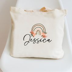 "If you're looking for a unique and personalized gift for your bridesmaids, look no further than our personalized tote bags! Each tote bag is made with your bridesmaid's name printed under a beautiful boho style rainbow. Not only are they a great way to show your appreciation for all their hard work on your big day, but they also make excellent giveaways for the bridal party at the reception. Order yours today and let us help you personalize it to perfection! 12 oz. 100% heavy cotton canvas. Product Size: 16\"W  x 14\"H x 3\"D Webbed handles Magnetic lock closure Machine washable, Eco-friendly, durable, recyclable Totes are perfect for carrying books, clothing, day care essentials, school supplies, toys etc, HOW TO ORDER:  1. Select the quantity range you would like to order. i.e if you ne Personalized Bags For Bridesmaid Gift, Personalized Bags For Mother's Day Gift, Customizable Rectangular Bag For Wedding Gift, Personalized Rectangular Bag With Custom Name, Rectangular Bag With Custom Name For Personalized Gift, Custom Name Rectangular Bag For Personalized Gift, Personalized White Bag For Wedding Gift, Cute White Bag For Personalized Gift, Toddler Tote Bag