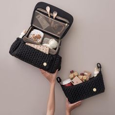 two people holding open black suitcases filled with food and utensils on top of a table