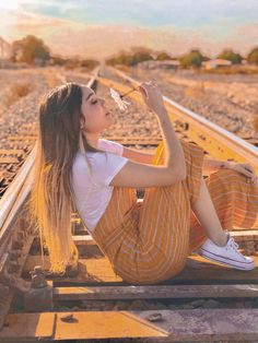 a woman sitting on the train tracks drinking from a wine glass and looking up at the sky