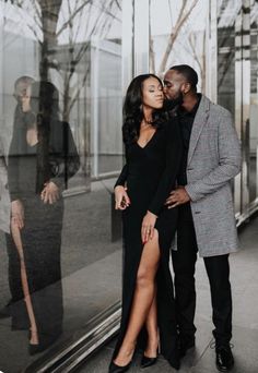 a man and woman standing next to each other in front of a glass wall kissing