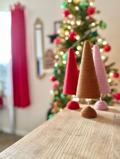 three small christmas trees sitting on top of a wooden table next to a christmas tree