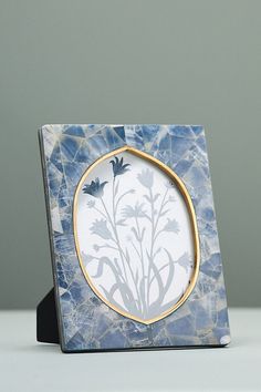 a blue and white photo frame with flowers in the center, on a table next to a gray wall