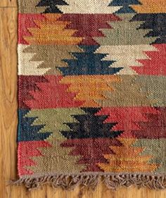 a multicolored rug with fringes on top of a wooden floor next to a wall