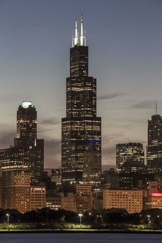 the city skyline is lit up at night, with skyscrapers in the foreground