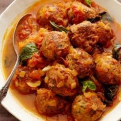 a white plate topped with meatballs covered in tomato sauce and garnished with basil