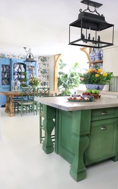 a green kitchen island in the middle of a white floored room with blue cabinets