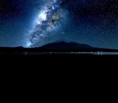 the night sky is filled with stars and milky above mountains, as well as water