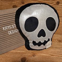 a black and silver skull pillow sitting on top of a wooden table next to a sign