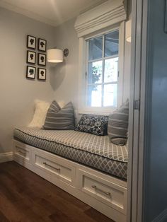 a window seat with pillows on it in front of a wooden floor and white walls