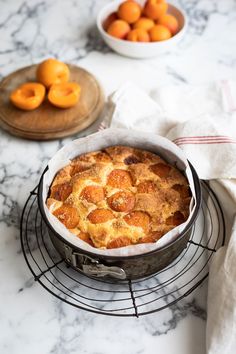 a cake sitting on top of a wire rack next to bowls of oranges in the background