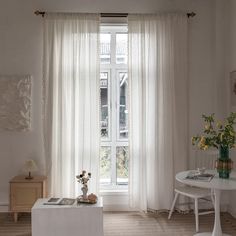 a living room with white furniture and curtains on the windowsills, along with flowers in vases