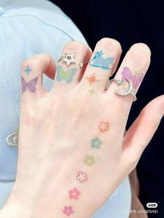 a woman's hand with several different colored tattoos on her left thumb and fingers