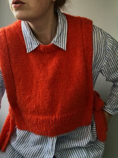 a woman wearing an orange sweater vest and striped shirt