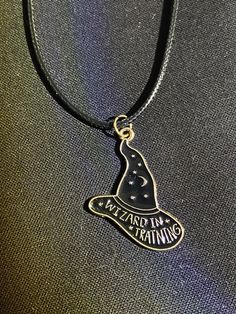 "Wizard in Training" Leather Cord Necklace  Enamel charm necklace, with leather cord.  Great alternative gift, Halloween accessory or year round accessory!  Strong cord and durable charm! Alternative jewellery, alternative necklace, witches necklace, wizards necklace, wizard in training necklace, witch in training necklace, leather cord necklace, faux leather cord necklace, Halloween necklace, Halloween gift, Halloween accessory. Adjustable Black Themed Necklace, Adjustable Nickel Free Halloween Necklaces, Adjustable Black Spiritual Charm Necklaces, Black Adjustable Spiritual Charm Necklace, Handmade Adjustable Witchy Necklaces, Adjustable Magical Pendant Jewelry, Magical Adjustable Pendant Necklace, Adjustable Black Charm Necklace, Adjustable Black Necklace With Charms