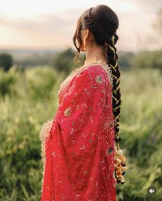 a woman with braids in a red dress looking off into the distance while standing in tall grass