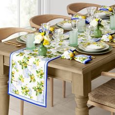 the table is set with yellow and white flowers on it, along with green vases