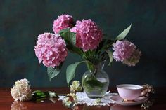 a vase filled with pink flowers sitting on top of a table next to a cup and saucer