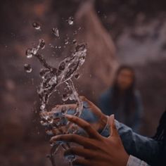 a woman holding an object with water splashing out of it's palm and hands