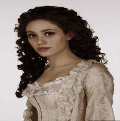 a woman with long curly hair wearing a white dress and posing for a photo in front of a white background