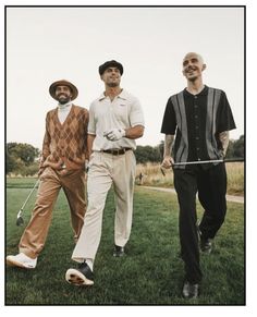 three men are walking in the grass with their golf clubs and one is wearing a hat