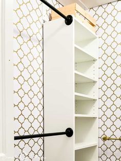 a white closet with shelves and black handles in a room that has gold patterned wallpaper on the walls