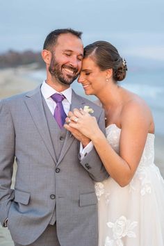 a bride and groom standing next to each other on the beach smiling at each other