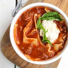 a white bowl filled with pasta and sauce on top of a wooden cutting board next to a spoon