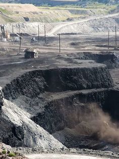 an open pit in the middle of a dirt field with trucks and machinery behind it