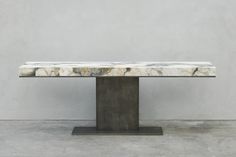 a marble table sitting on top of a metal stand in front of a gray wall