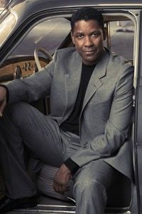 a man in a suit sitting on the door of a car with his legs crossed