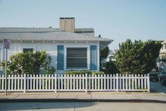 a white picket fence sits in front of a blue and white house with cars parked on the street