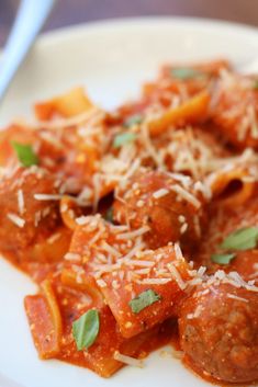 a white plate topped with meatballs covered in tomato sauce and parmesan cheese