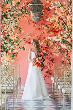 a bride standing in front of an orange and pink backdrop with flowers on the wall