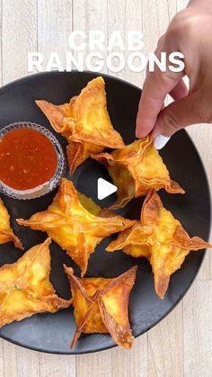 a person dipping sauce on top of some fried food items in a black plate with the words crab rangoons above it