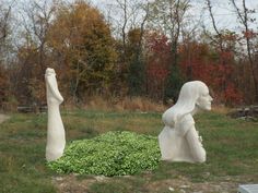 two white sculptures sitting on top of a grass covered field next to trees and bushes