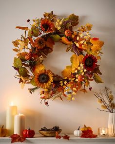 a wreath with sunflowers and autumn leaves is hanging on the wall next to candles