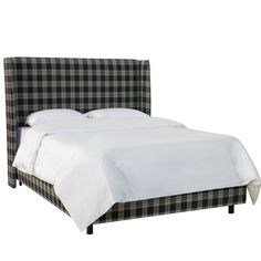 a bed with white sheets and plaid headboard