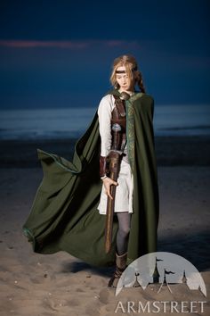 a woman dressed in medieval clothing standing on the beach at night with her cape draped over her head