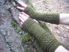 a person wearing green knitted arm warmers standing next to a tree trunk with moss growing on it