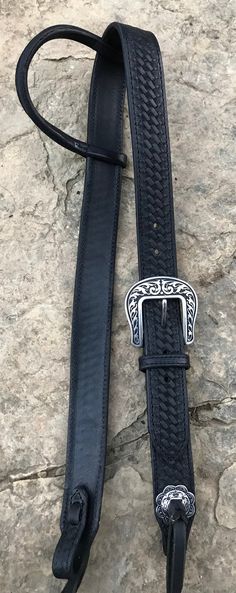 a black leather belt with a silver buckle on it sitting on top of a rock