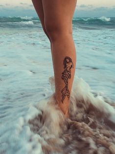 a woman's foot with a tattoo on it walking in the water at the beach