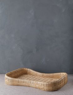 a rectangular wicker tray with handles on a table next to a gray wall and floor