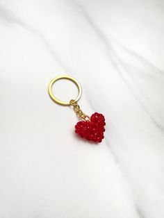 a red heart shaped keychain on a white marble surface with a gold ring