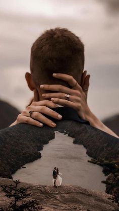 a man covering his face with both hands while standing on top of a mountain next to a river