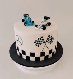 a white cake with black and white checkered design on the top is topped with a racing car