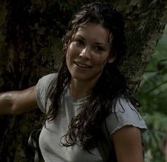 a woman standing next to a tree in the woods