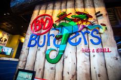 the sign for burgers bar and grill in front of a wooden wall with neon signs on it