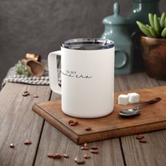 a white coffee mug sitting on top of a wooden cutting board next to a spoon